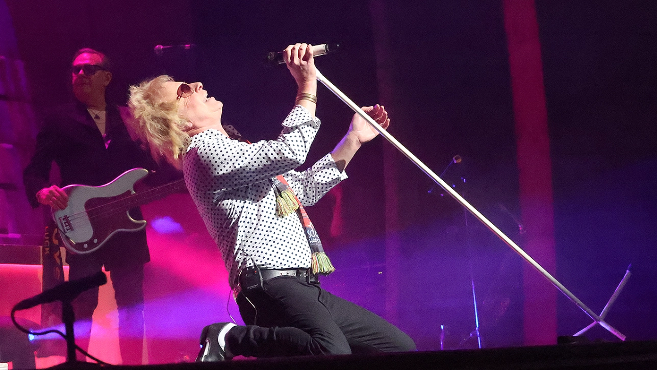 Paul Metcalfe performing as Sir Rod Stewart kneeling on stage with a microphone 