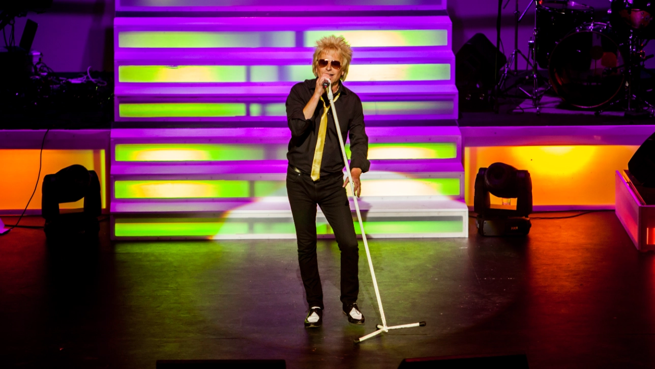 Paul Metcalfe as Sir Rod Stewart holding a microphone on stage 